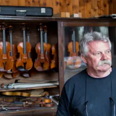 Mistrz lutnik, który robi skrzypce, stoi obok gabloty pełnej instrumentów.