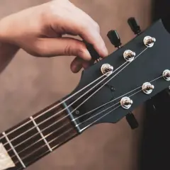 Dłoń kręci kluczem przy główce gitary elektrycznej, pokazując jak nastroić gitarę elektryczną bez stroika, słuchając dźwięku.