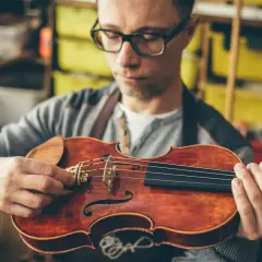 Mężczyzna w okularach sprawdza, ile strun ma skrzypce. Instrument ma cztery struny.