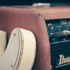 Biała gitara elektryczna podłączona do wzmacniacza Ibanez. Idealny zestaw, by dowiedzieć się, jak zacząć grać na gitarze elektrycznej.