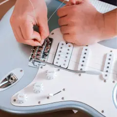 Ręce montują nową strunę w gitarze elektrycznej. Dowiedz się, co ile wymieniać struny w gitarze elektrycznej, by cieszyć się czystym brzmieniem.