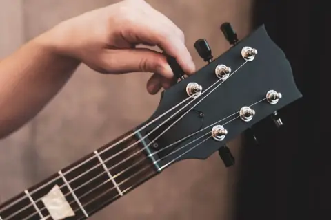 Dłoń kręci kluczem przy główce gitary elektrycznej, pokazując jak nastroić gitarę elektryczną bez stroika, słuchając dźwięku.