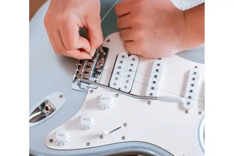 Ręce montują nową strunę w gitarze elektrycznej. Dowiedz się, co ile wymieniać struny w gitarze elektrycznej, by cieszyć się czystym brzmieniem.