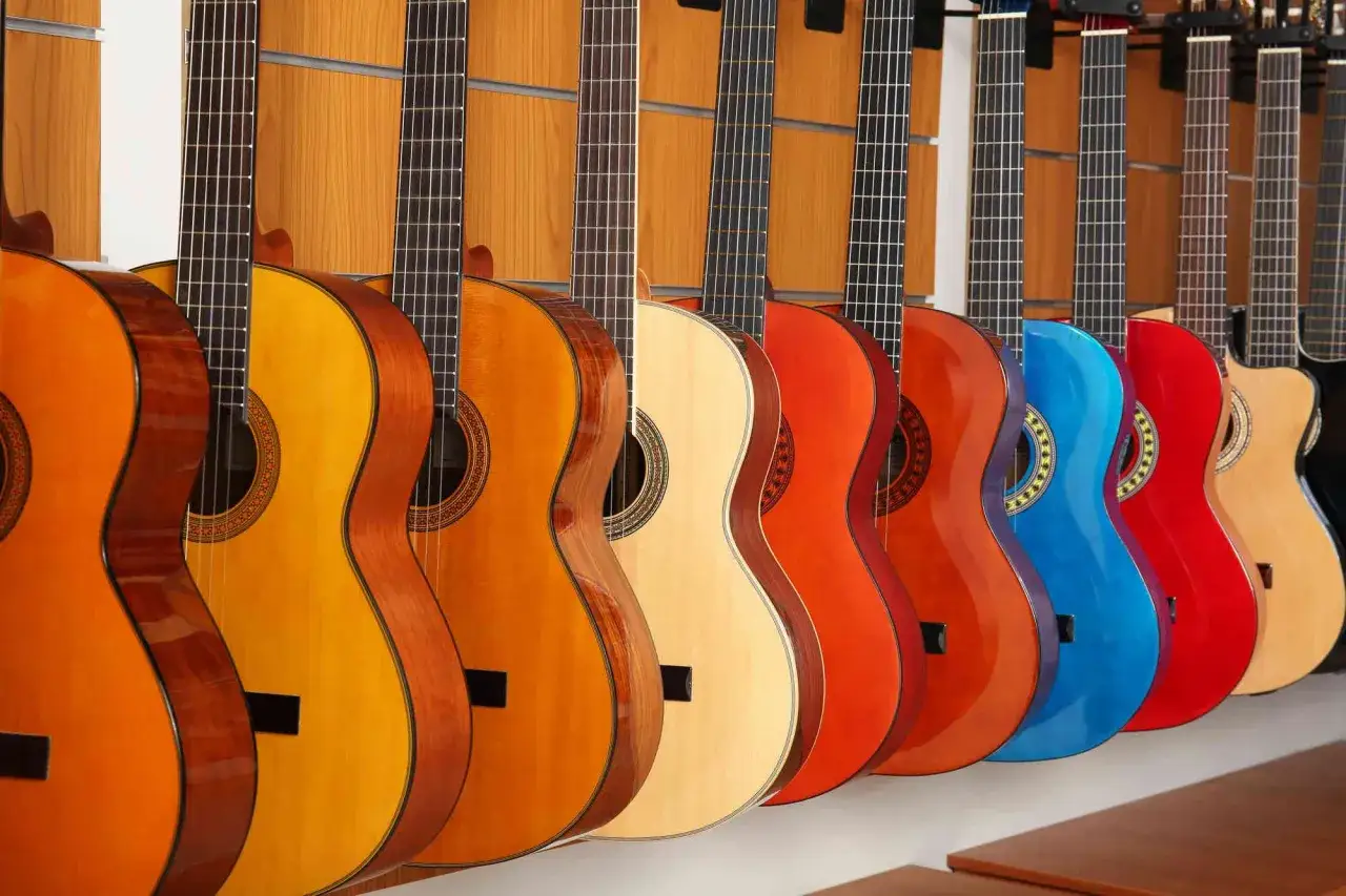 Rząd gitar akustycznych w różnych kolorach i rozmiarach, od naturalnego drewna po jaskrawy niebieski i czerwony.