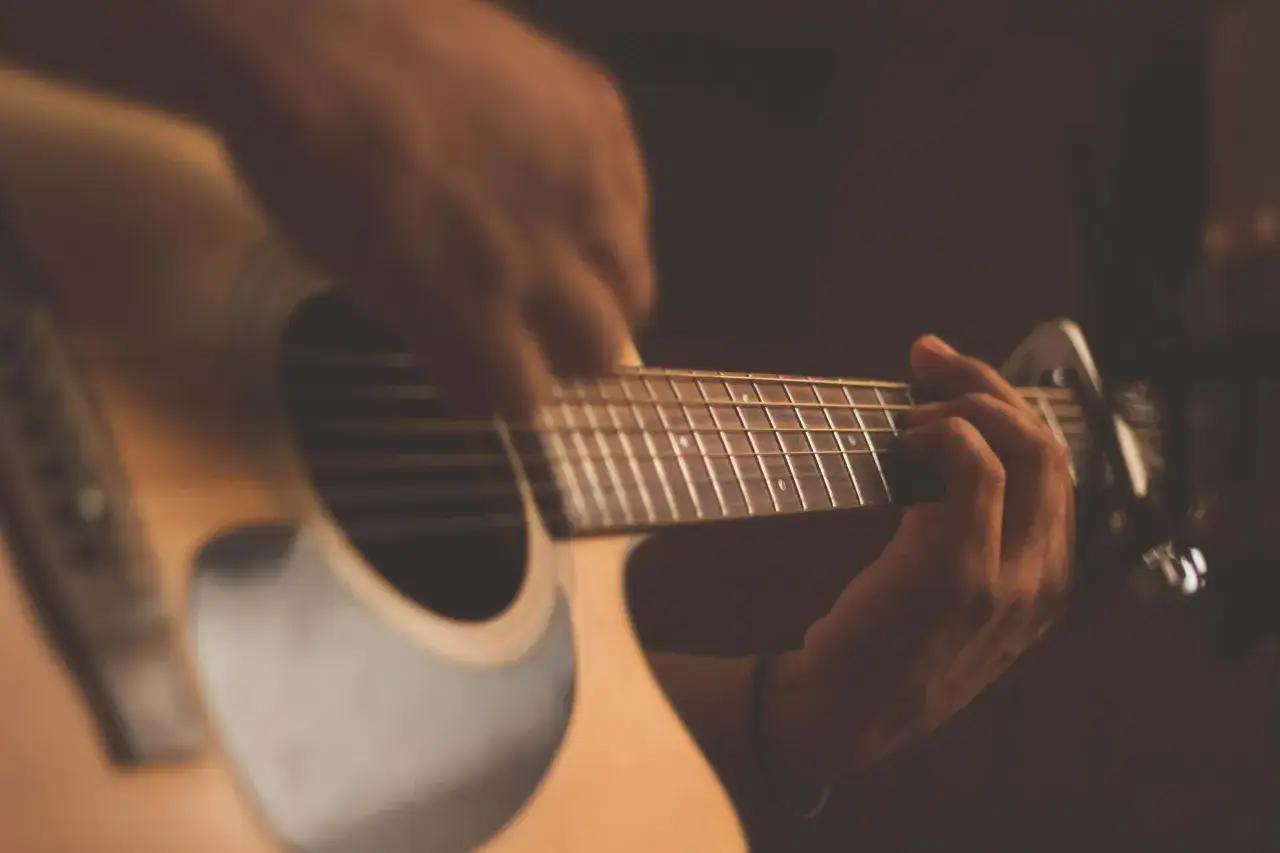 Ręce grające na gitarze, z widocznym stroikiem. Dowiedz się, jak używać stroika do gitary, by ułatwić sobie grę.