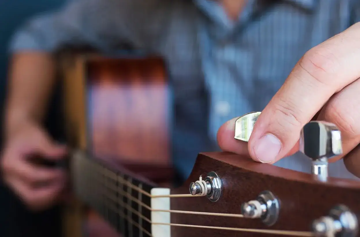 Dłoń z kostką do gitary kręci kluczem, by nastroić instrument. Poznaj, jak używać stroika do gitary, by uzyskać idealne brzmienie.