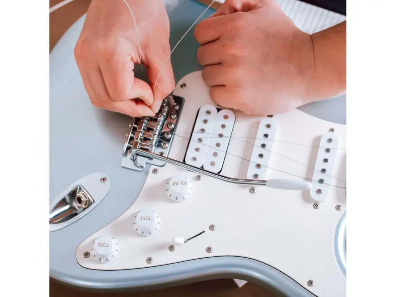 Ręce zakładają nową strunę do gitary elektrycznej. Dowiedz się, co ile wymieniać struny w gitarze elektrycznej, by brzmiała jak nowa.